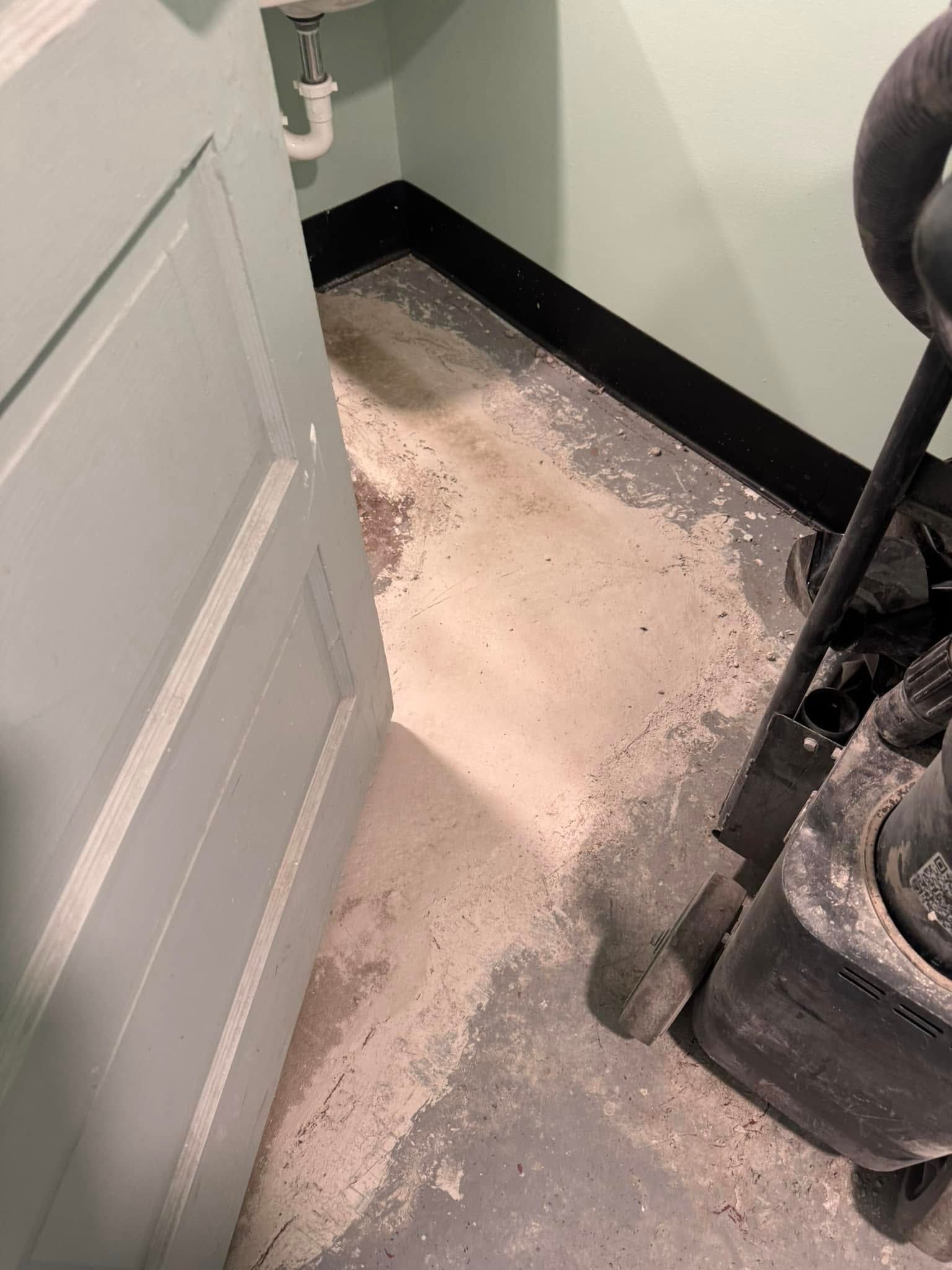 A view inside a room showing worn, gray concrete flooring near a sink, a door, and a black baseboard.