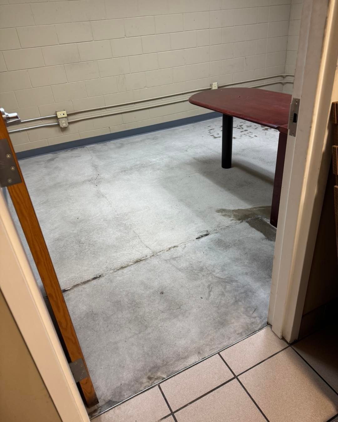 A small office with bare concrete floors and a single maroon table, viewed through an open doorway.