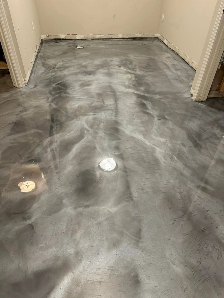 A room with a polished, metallic gray epoxy floor featuring swirling patterns and two circular floor drains.