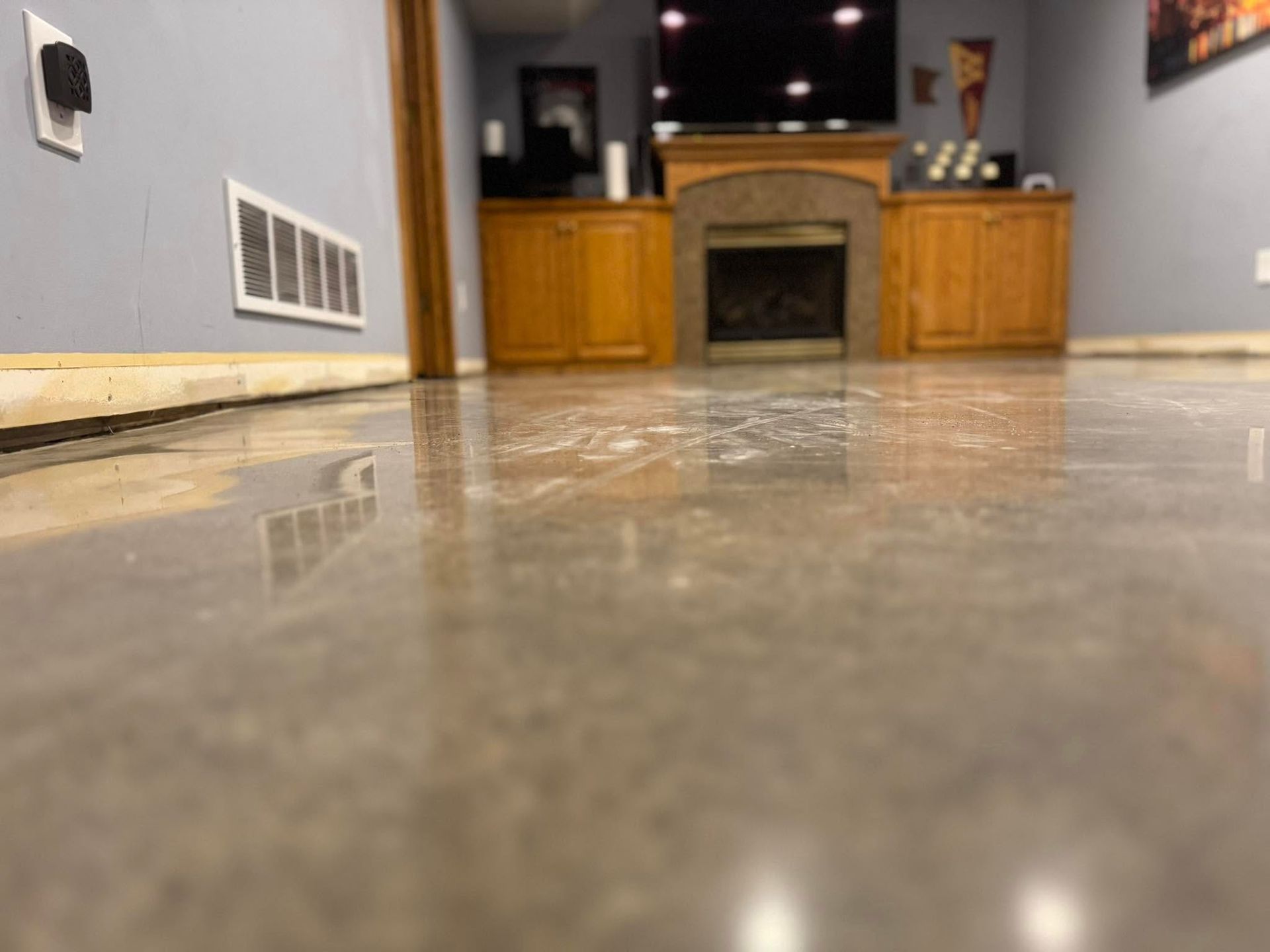 A low-angle view of a polished concrete floor in a room with light blue walls, a fireplace, and built-in wood cabinets.
