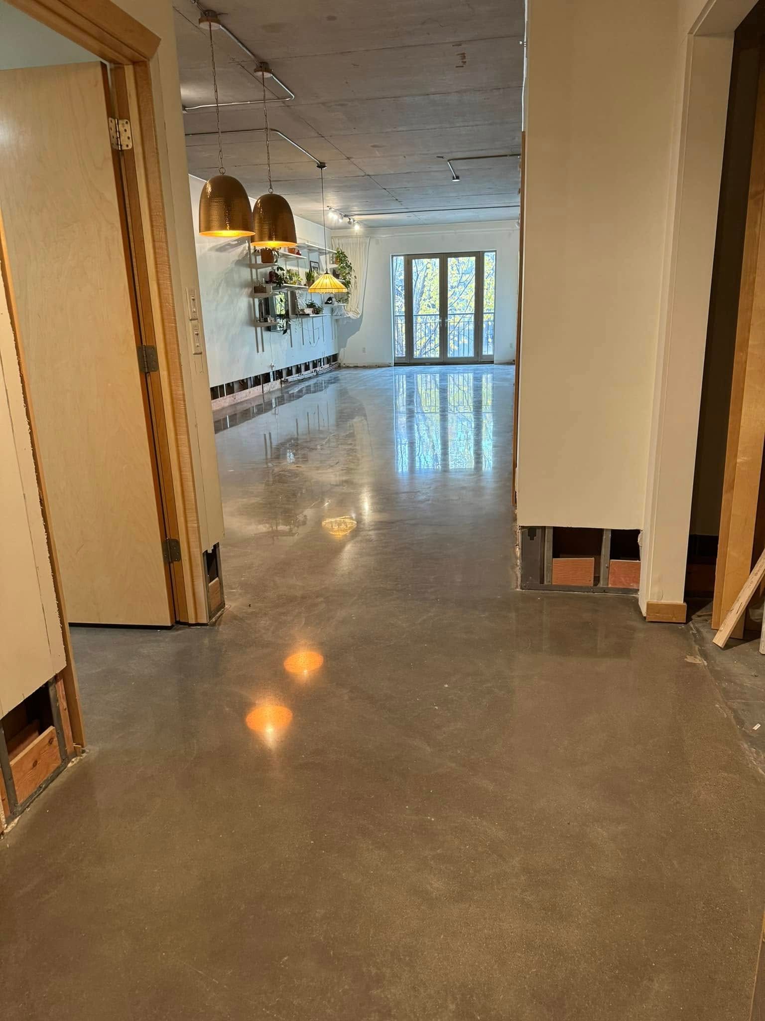 A polished concrete hallway leads past wooden door frames toward a distant doorway and hanging pendant lights.