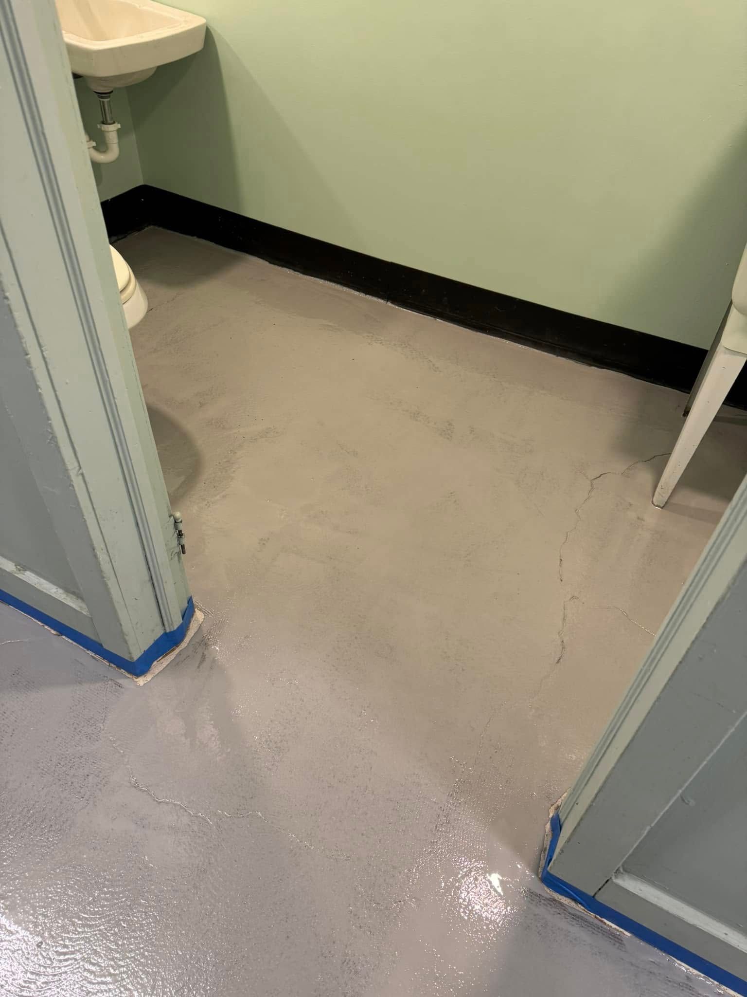 An interior shot shows a freshly painted gray floor meeting a doorway, with a pedestal sink visible in the background.