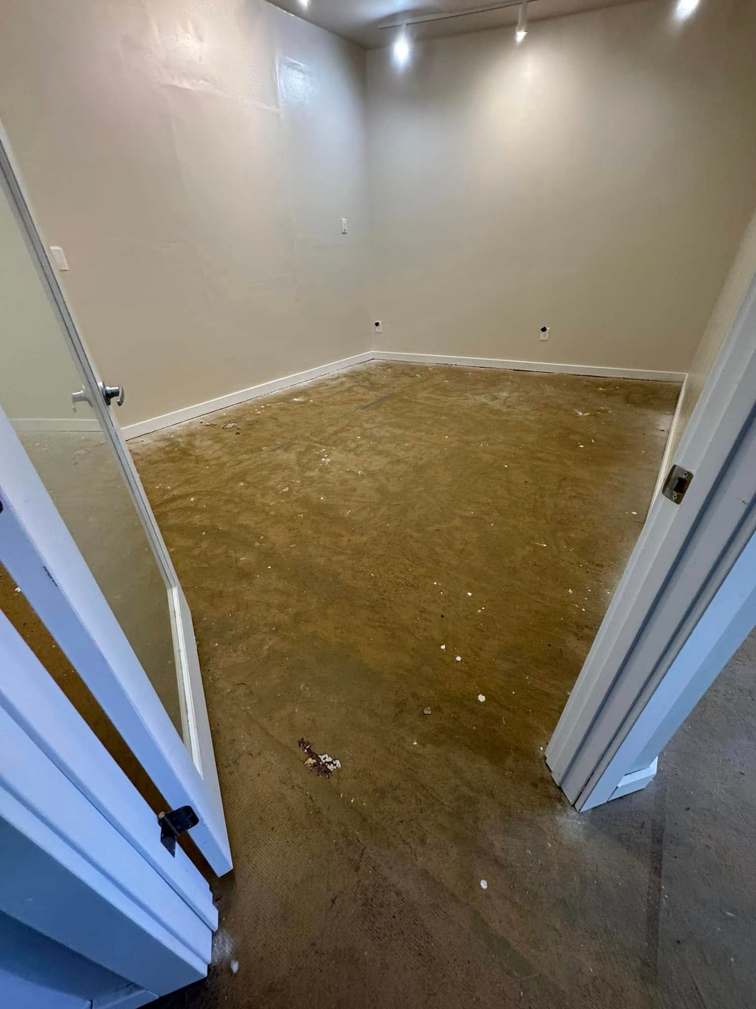 An empty room with beige walls and a brown carpet, viewed through an open doorway.