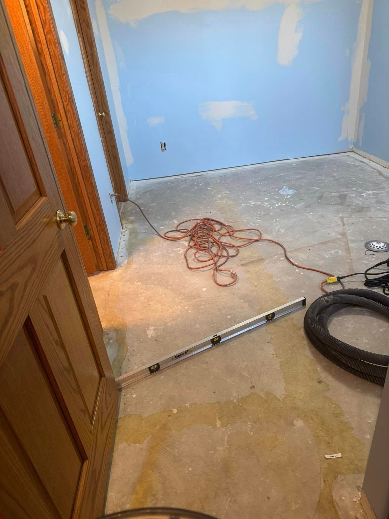 A room under renovation with light blue walls, a concrete floor, a level tool, an extension cord, and a vacuum hose.