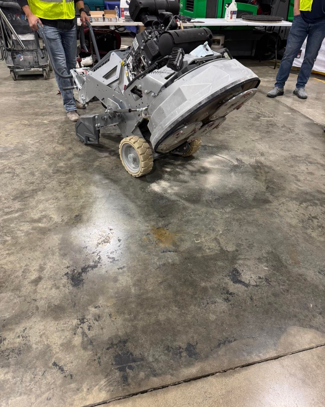 A construction worker using a large industrial floor grinder to polish a concrete surface in an indoor facility.