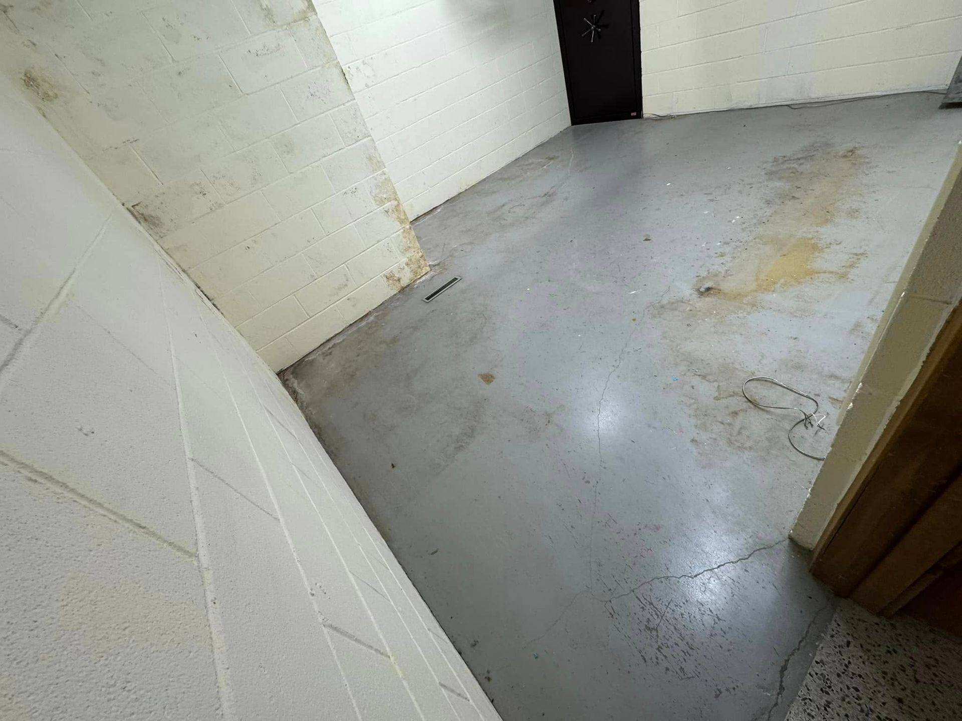 A grey concrete floor in an unfinished room with white block walls and a dark doorway in the background.