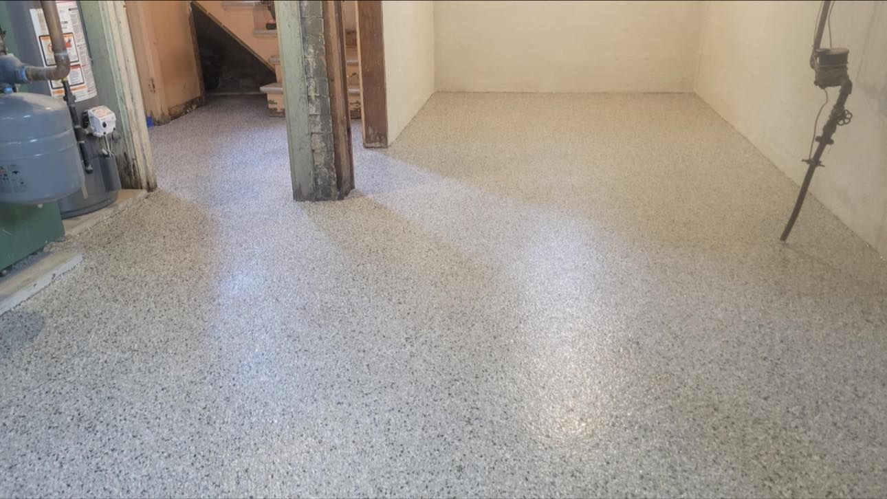 A basement with a freshly applied light-colored, speckled epoxy floor finish extending into an adjacent room.