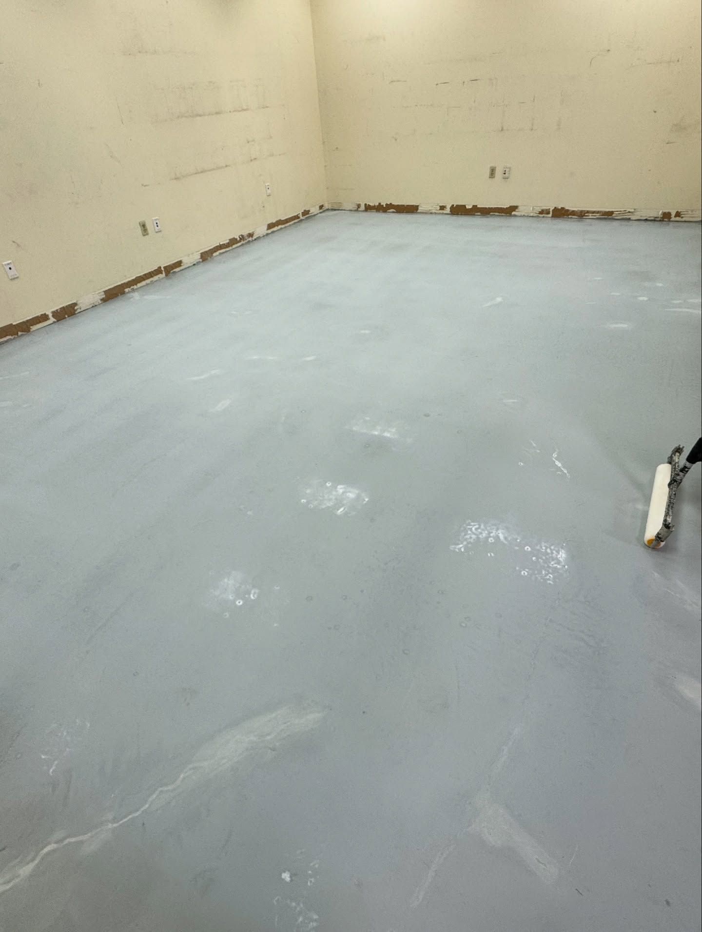 A gray primer-coated floor in an unfinished room with a paint roller resting on the right side.