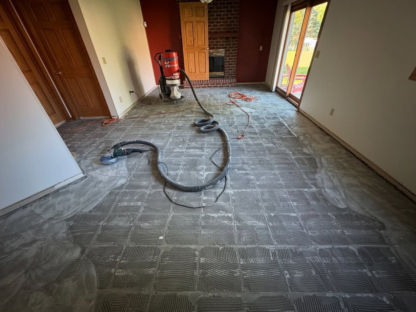 An interior room undergoing floor renovation, showing exposed subflooring with adhesive ridges and a vacuum tool.