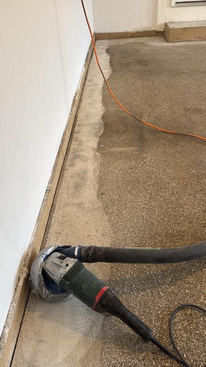 An angle grinder with a dust shroud and vacuum attachment smooths the edge of a concrete floor along a wall.