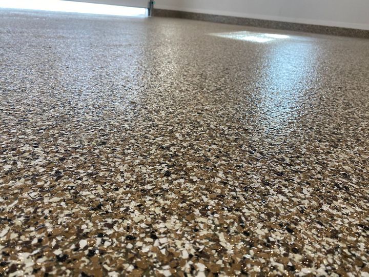 A close-up view of a high-gloss, epoxy garage floor with a multi-colored fleck pattern of tan, brown, black, and white.