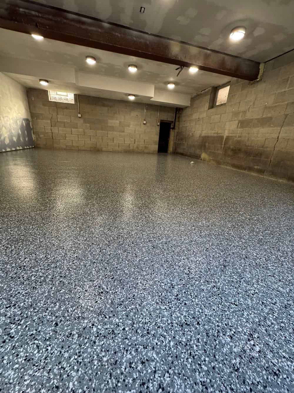 A finished basement with gray and white speckled epoxy flooring, concrete block walls, and recessed lighting.