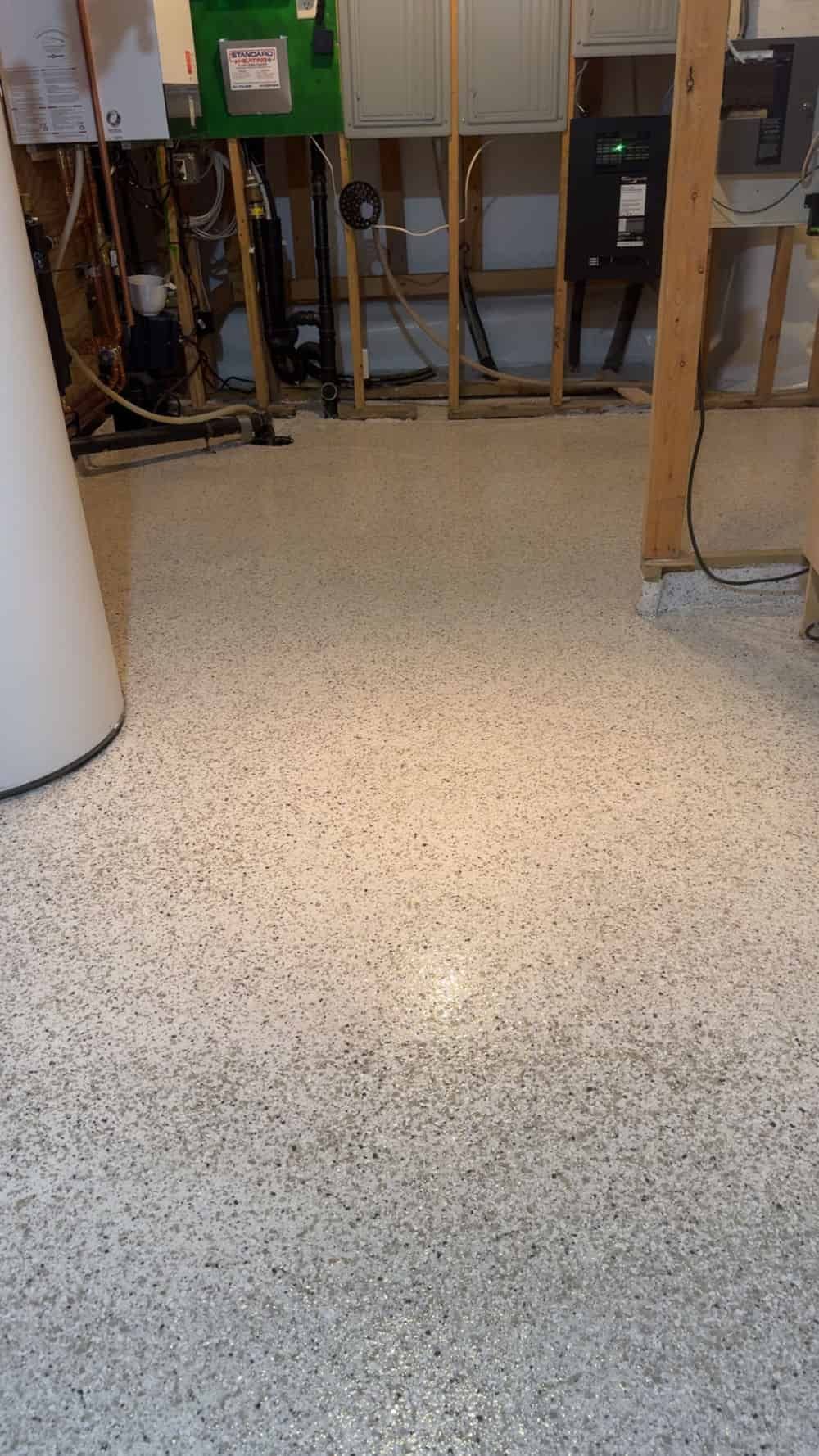 A room with a newly applied white and gray speckled epoxy floor, showing unfinished walls and electrical utility equipment.