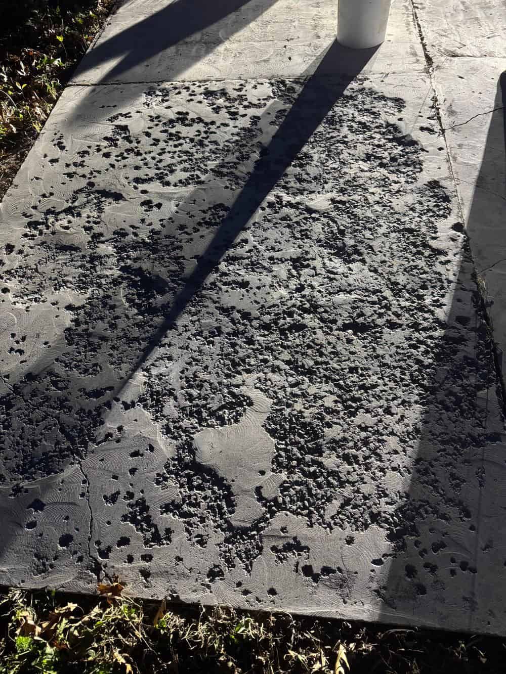 Gray concrete surface with deep, textured pitting, partially covered by the shadow of an object.