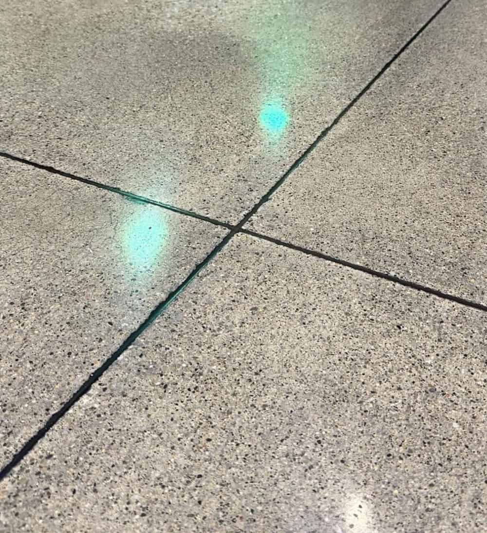 Light blue, glowing spots reflect on a textured grey floor marked by dark, intersecting grout lines.