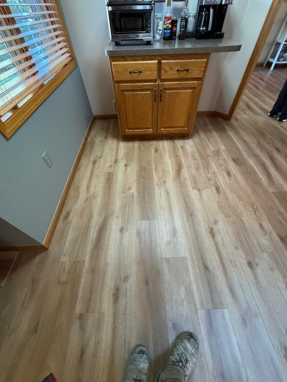 A first-person view of a wooden floor leading to a wooden cabinet with a microwave and coffee maker on top.