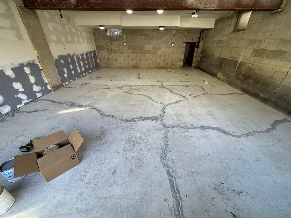 An unfinished concrete room with large cracks across the floor, a cardboard box, and partially painted walls.