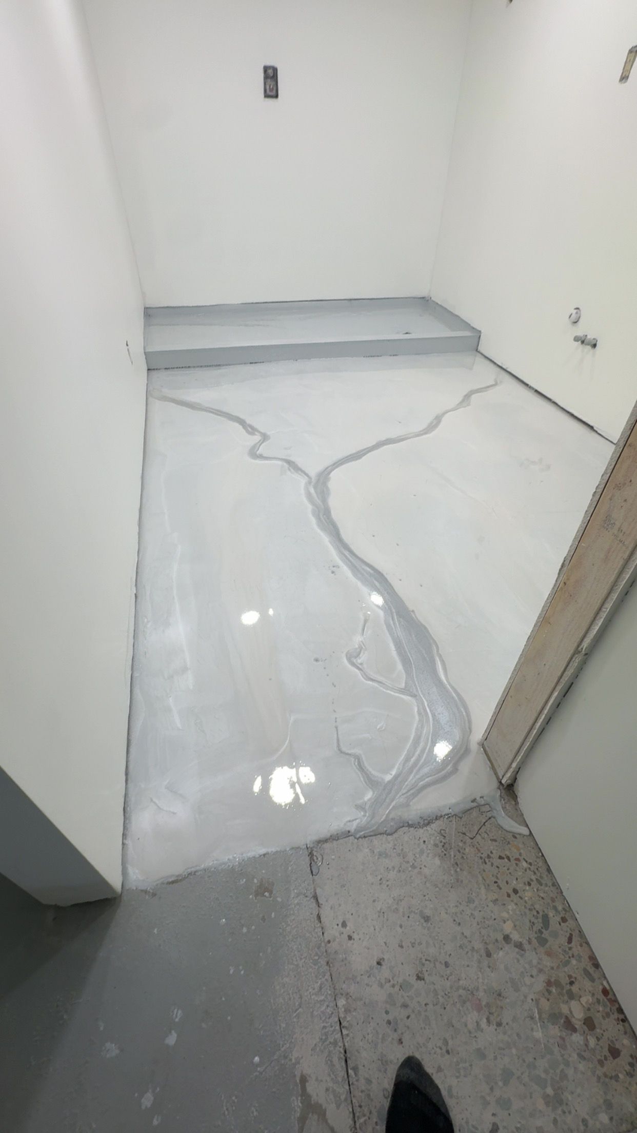 A light grey floor in a room, featuring a darker grey, river-like epoxy or paint design running across the surface.