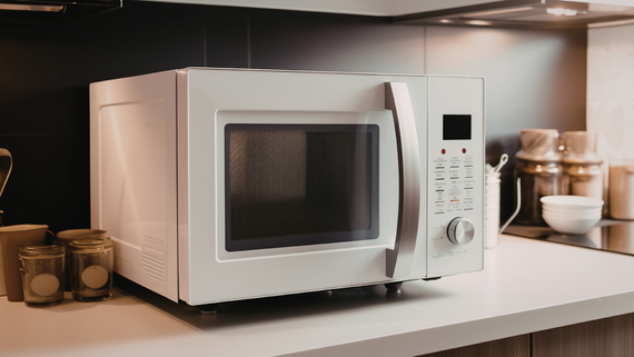 White microwave oven on a kitchen counter with jars and a kettle in the background