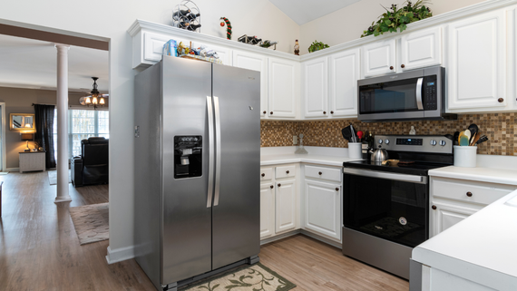 Bright kitchen with stainless steel fridge, white cabinets, black oven, and microwave