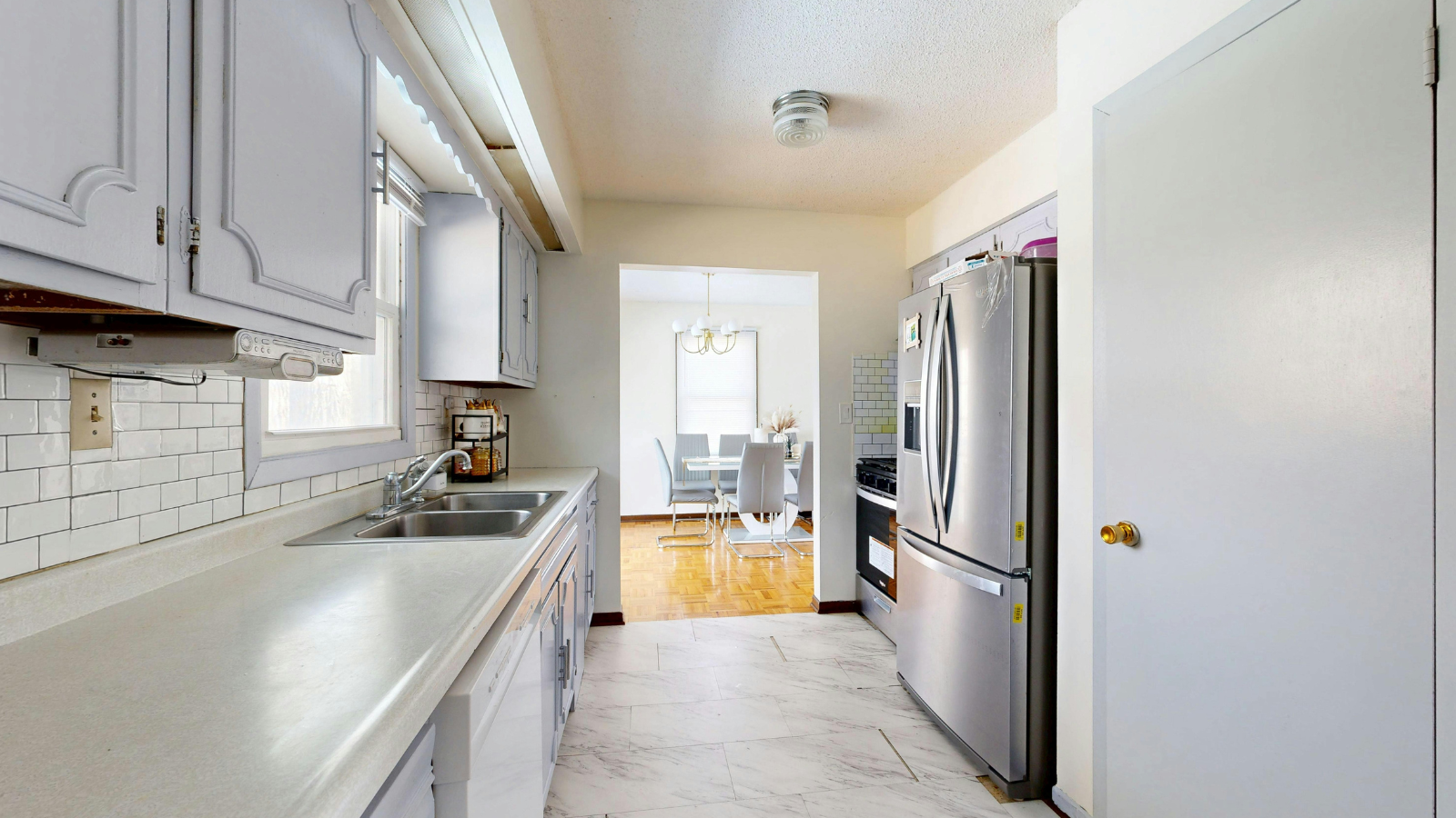 Bright kitchen with white cabinets, stainless fridge, and a view into a sunlit dining area.