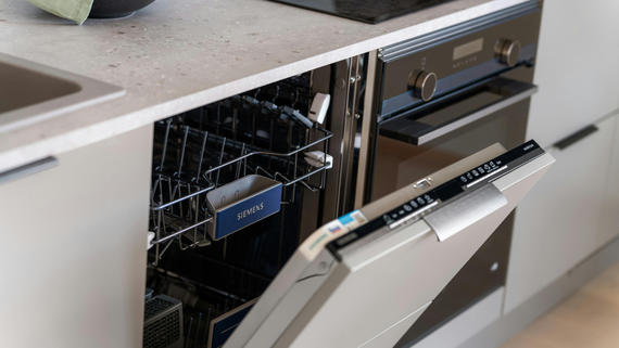 Open dishwasher with blue-labeled dish rack in a modern kitchen under a countertop