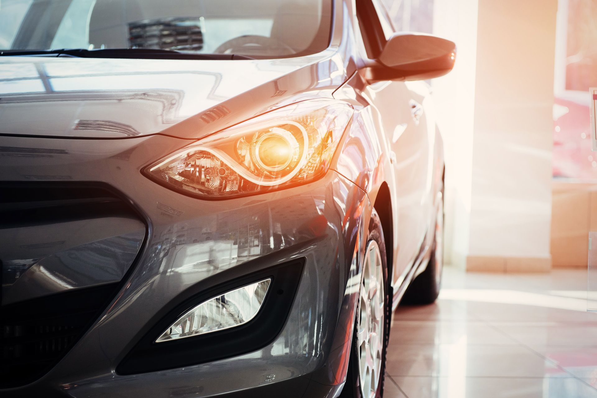 Silver car front end with headlights on in a bright showroom