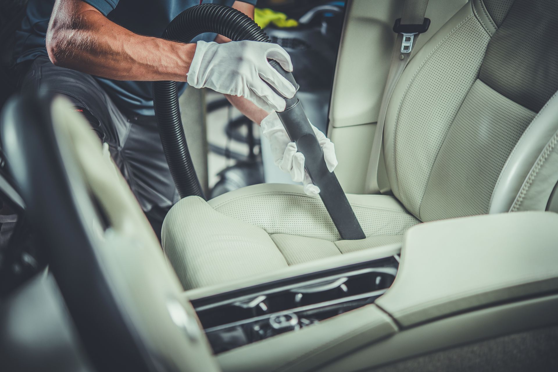 Person vacuuming a beige car seat and center console with a handheld cleaner Person vacuuming a beige car seat and center console with a handheld cleaner
