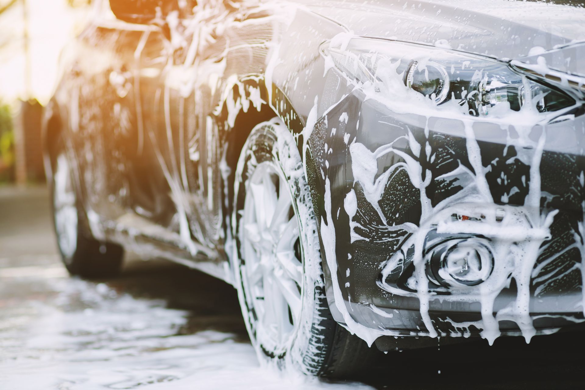 Car covered in thick white foam during a wash, with frothy soap on the wheels and body.
