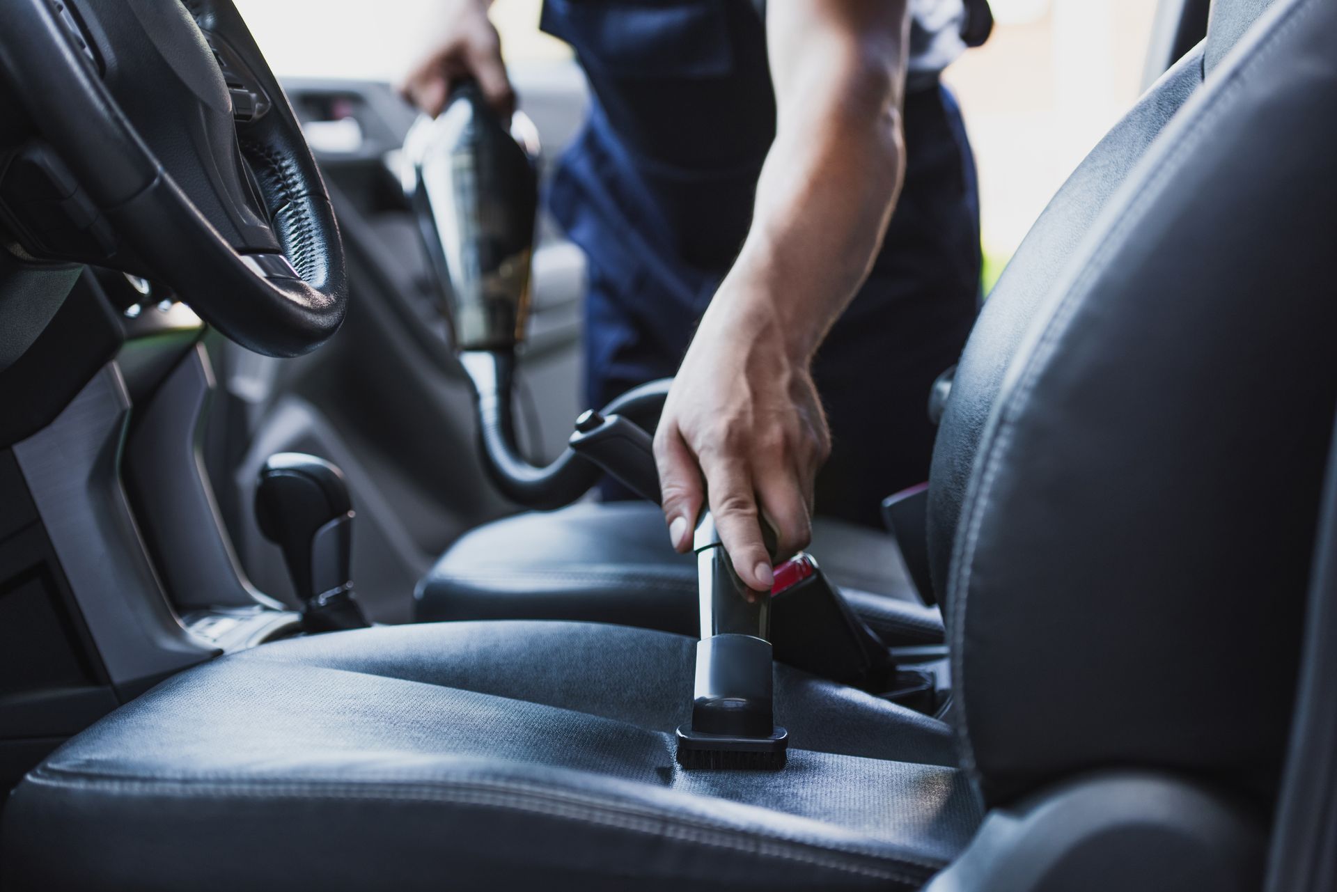 Hand vacuuming a car seat with a handheld cleaner and nozzle.