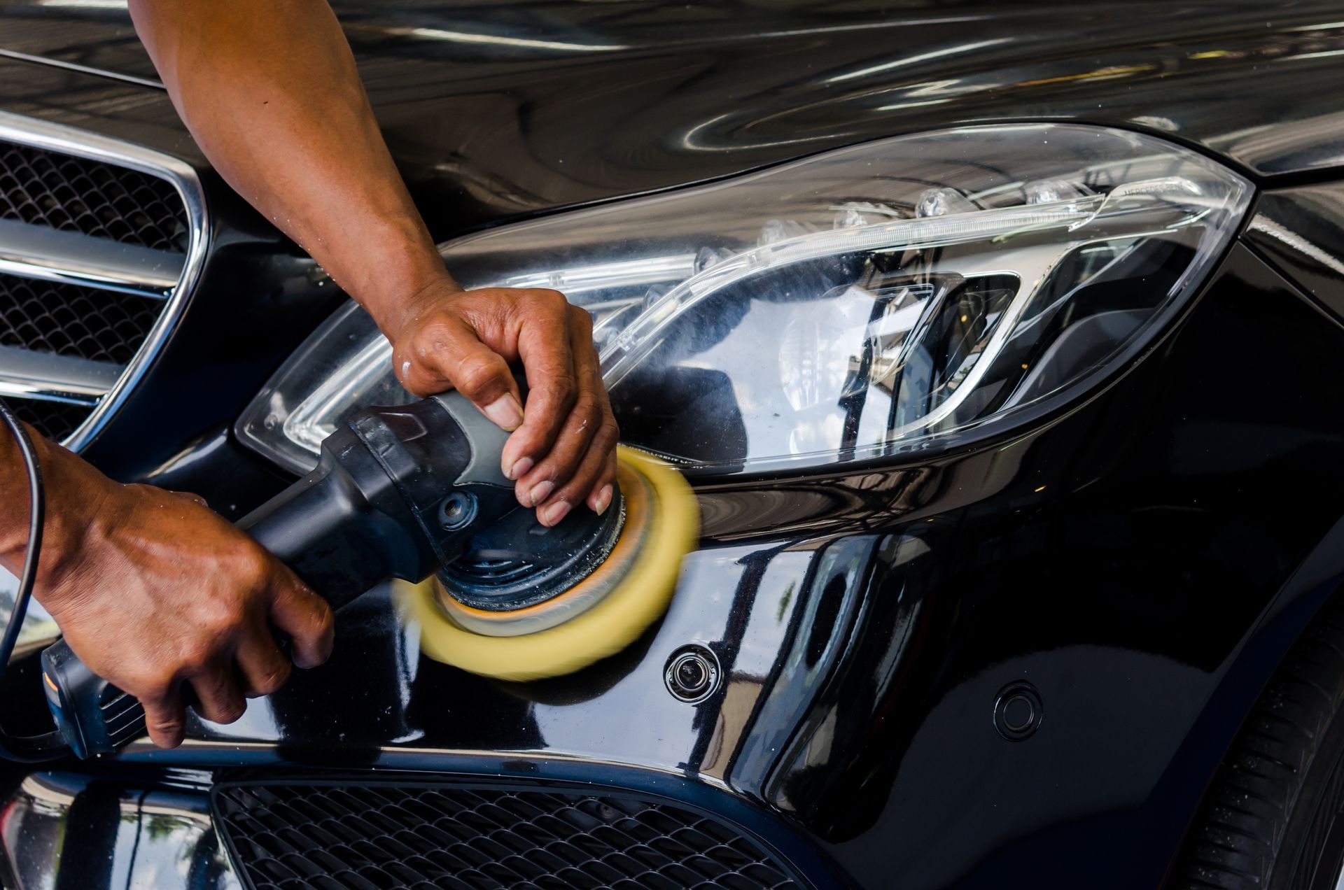 Person polishing a black car headlight with a buffing tool in a garage