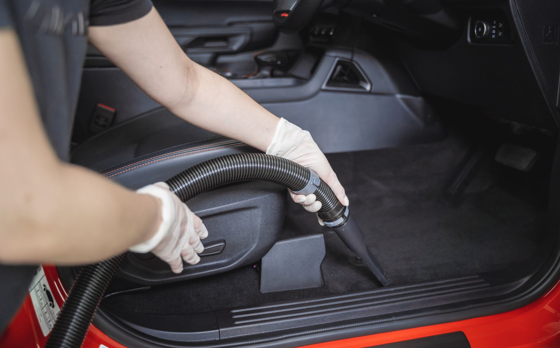 Person vacuuming the floor of a car interior with a handheld cleaner