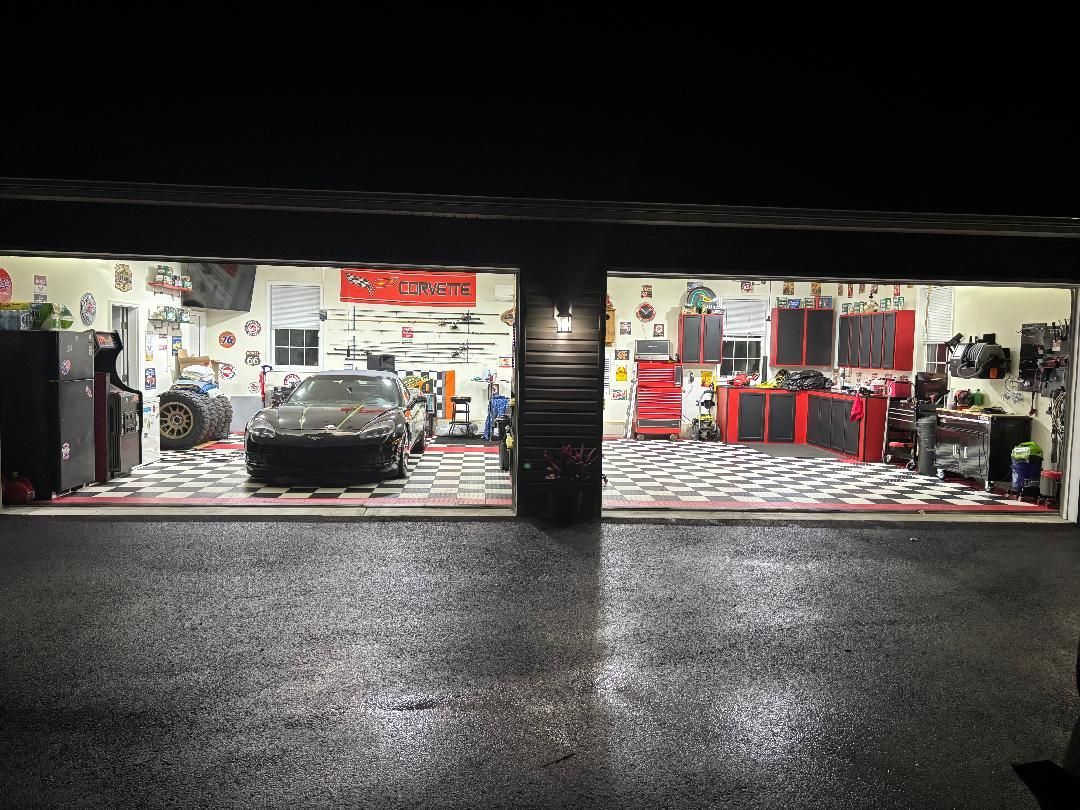 Two-car auto shop at night with red accents and a black car centered in the left bay