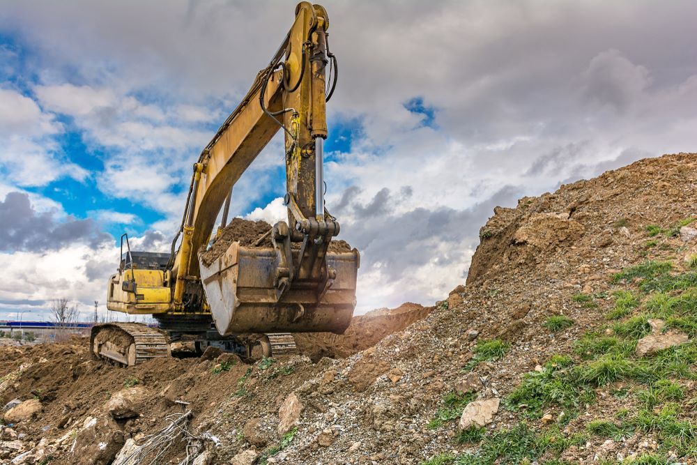 A Yellow Excavator is Moving Dirt on Top of a Pile of Rocks — STJ Earthmoving in Atherton, QLD