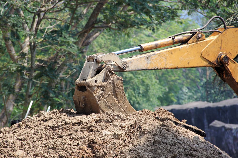 Yellow Excavator Bucket Scooping Up Brown Dirt — STJ Earthmoving in Kuranda, QLD