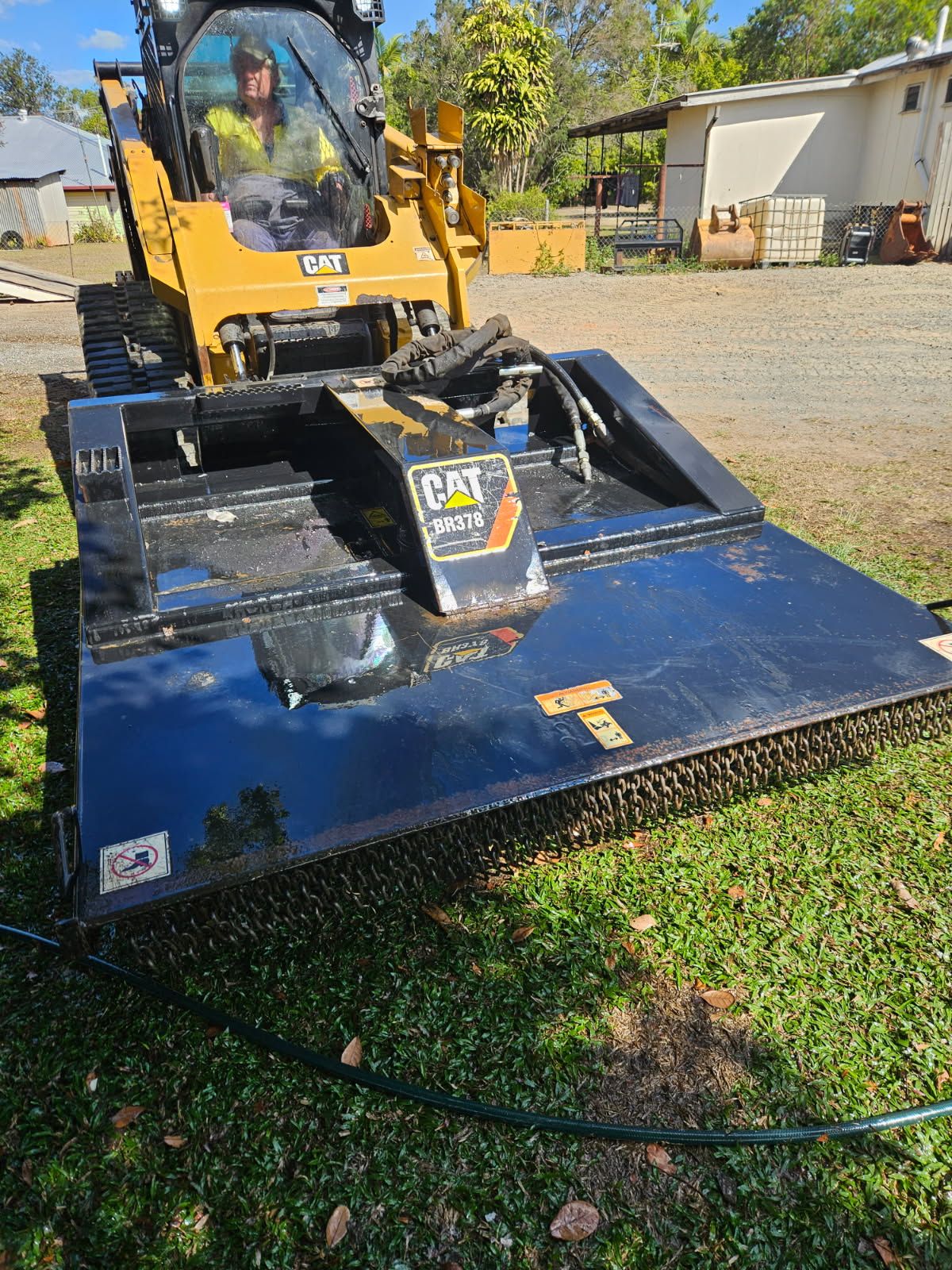 Yellow CAT Skid Steer with Brush Cutter Attachment on Grass — STJ Earthmoving in Georgetown, QLD