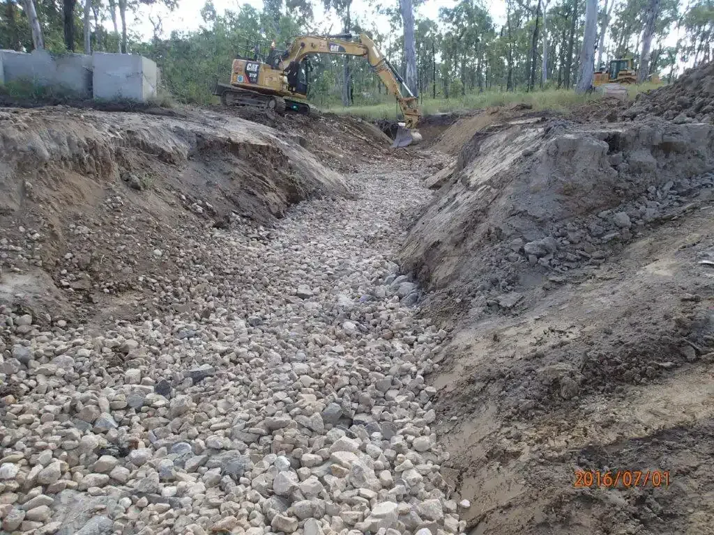 An Excavator Digs in a Gravel-filled Trench — STJ Earthmoving in Cooktown, QLD