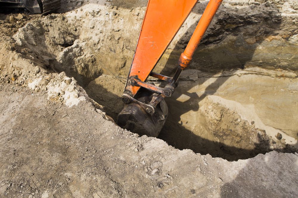 An Orange Excavator Bucket Digging a Trench in the Dirt — STJ Earthmoving in Musgrave, QLD