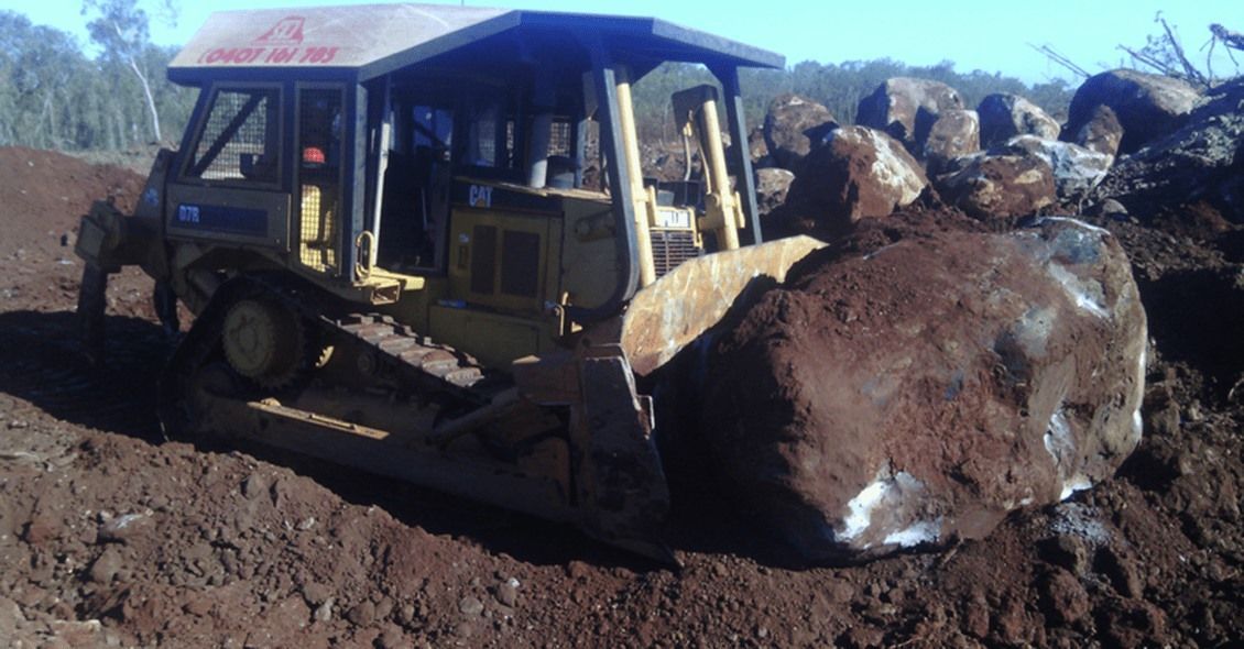 Yellow Bulldozer Pushing Large Rock on Dirt — STJ Earthmoving in Tully, QLD