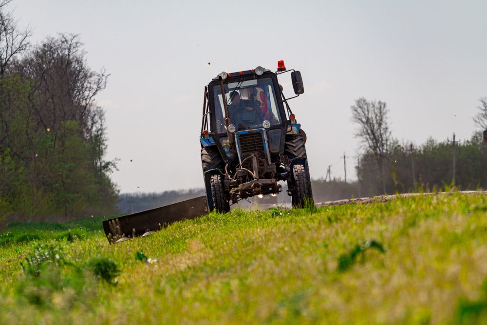 Blue Tractor Mowing Grass on a Grassy Embankment — STJ Earthmoving in Cooktown, QLD