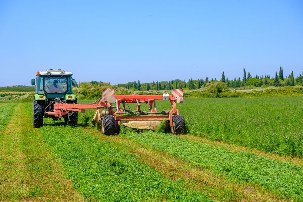 Tractor With Hay Rake Cutting a Field of Green Crop on a Sunny Day — STJ Earthmoving in Lakeland, QLD