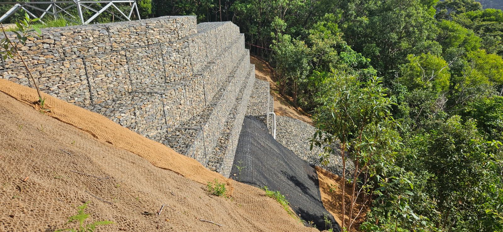 Stone Gabion Retaining Wall on a Hillside Next to Lush Green Vegetation — STJ Earthmoving in Archer River, QLD