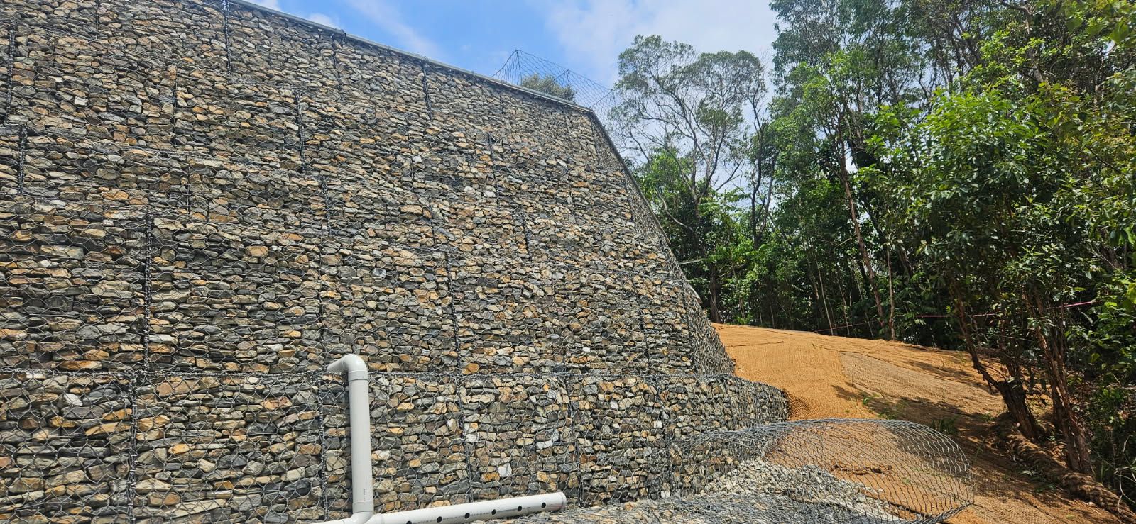 A Gabion Retaining Wall on a Hillside Next to Trees and a Dirt Path — STJ Earthmoving in Julatten, QLD