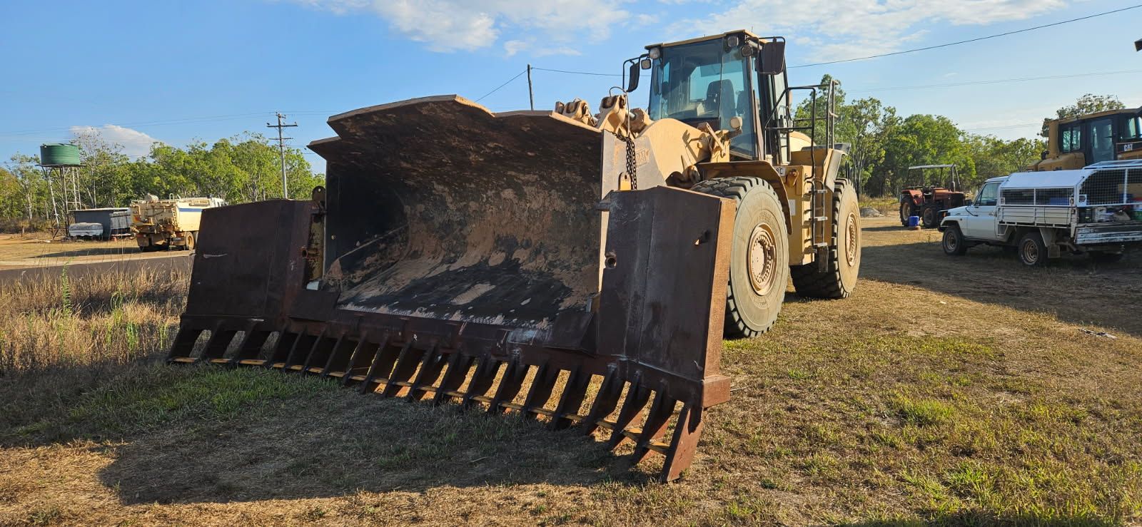 A Yellow Bulldozer With a Large Rake-like Bucket Stands in a Grassy Field — STJ Earthmoving in Mission Beach, QLD