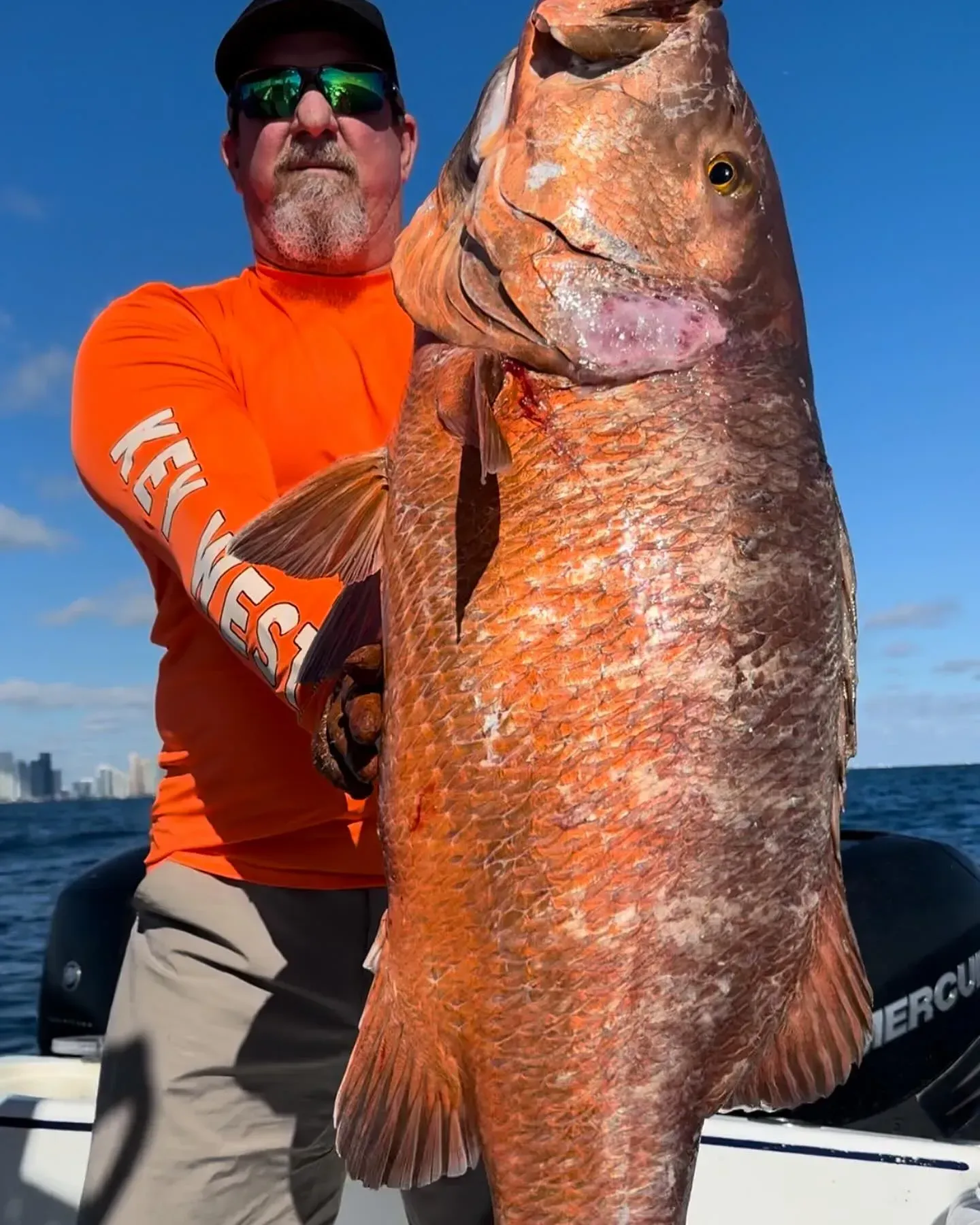 A man in an orange shirt is holding a large fish
