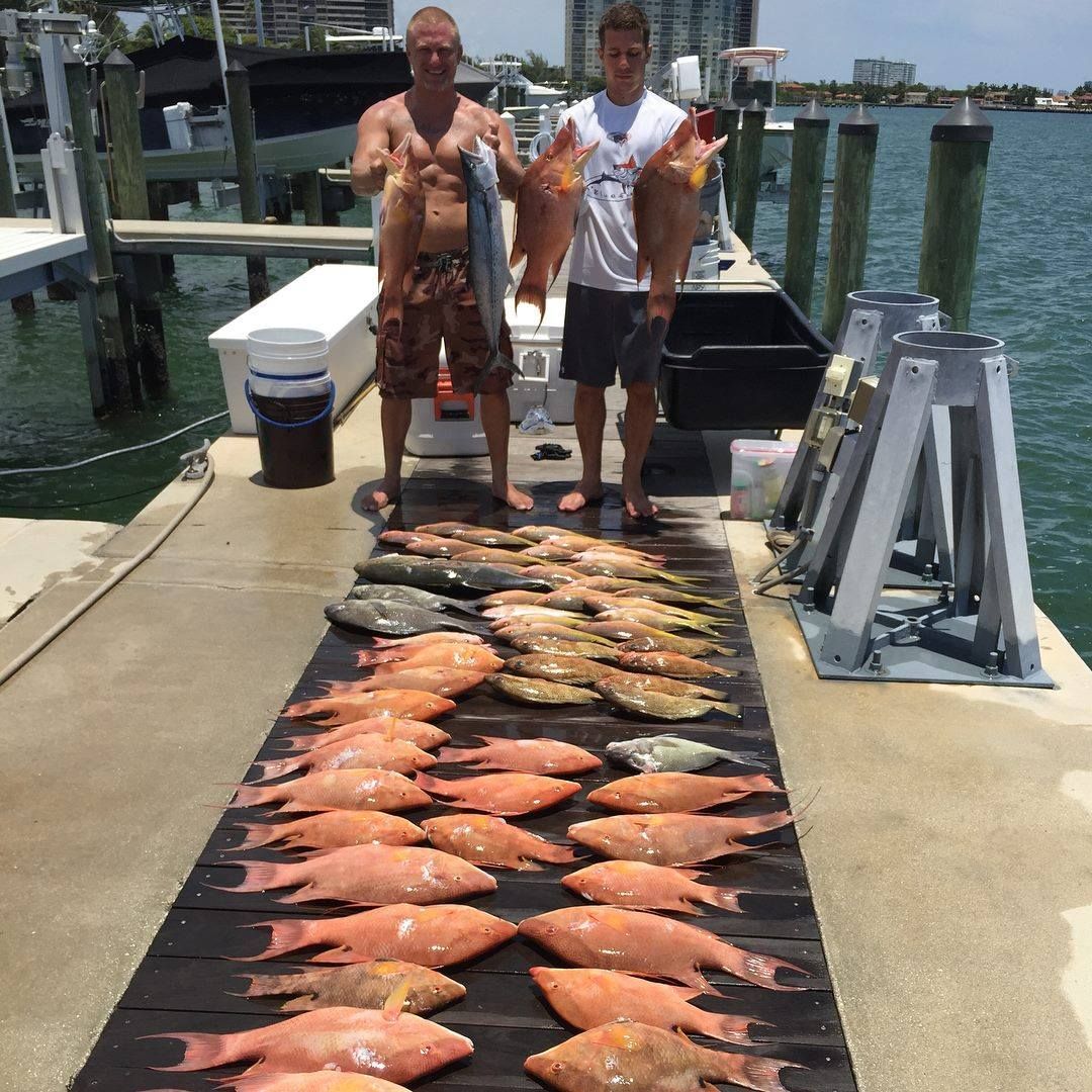 Two men are standing on a dock holding fish