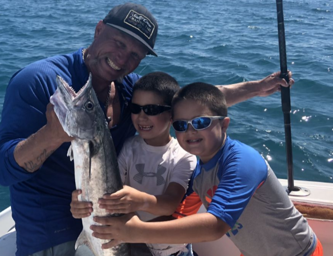 A man and two boys are holding a large fish on a boat.