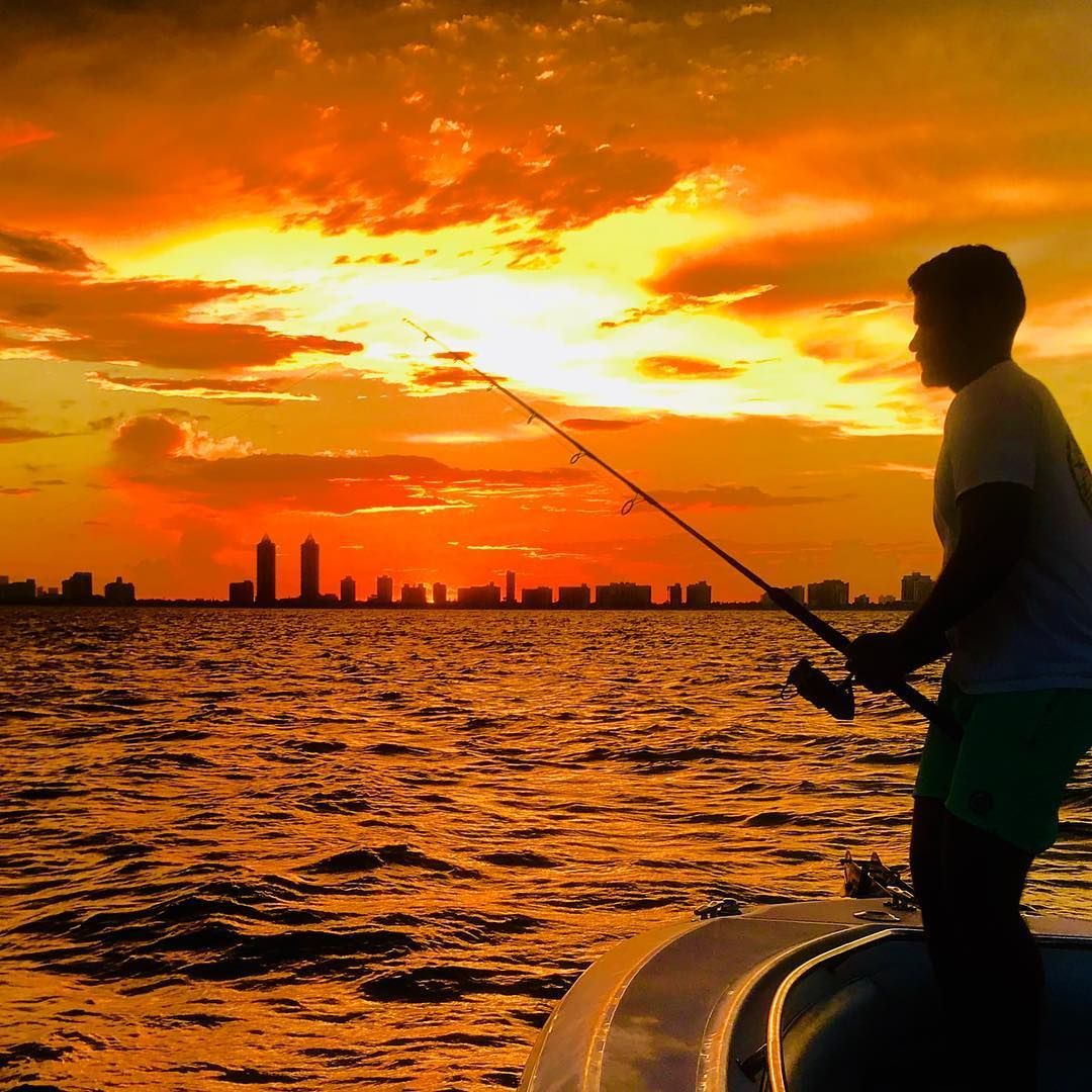 A man is fishing in the ocean at sunset