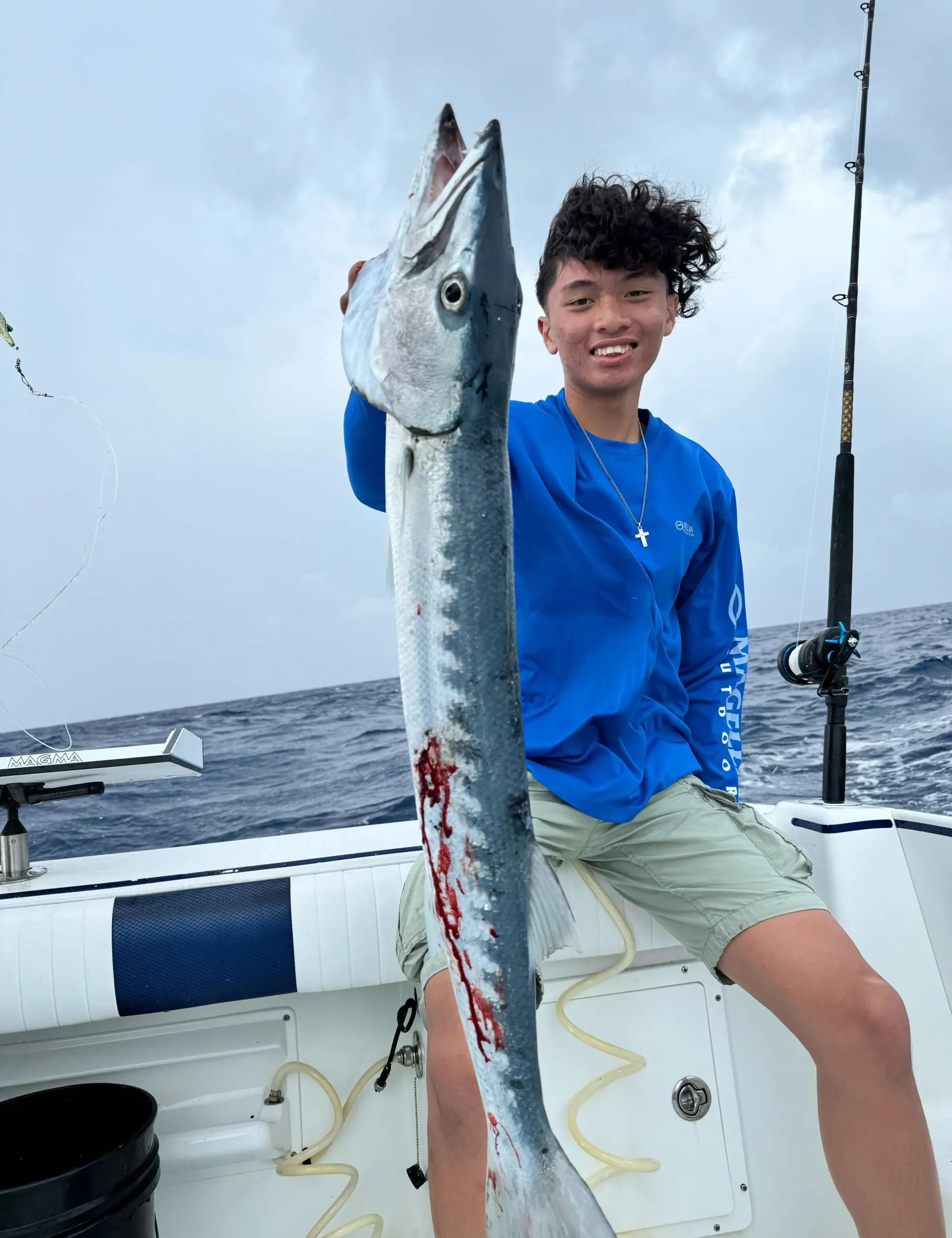 A young man is sitting on a boat holding a large fish.