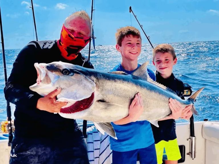 A man and two boys are holding a large fish on a boat.